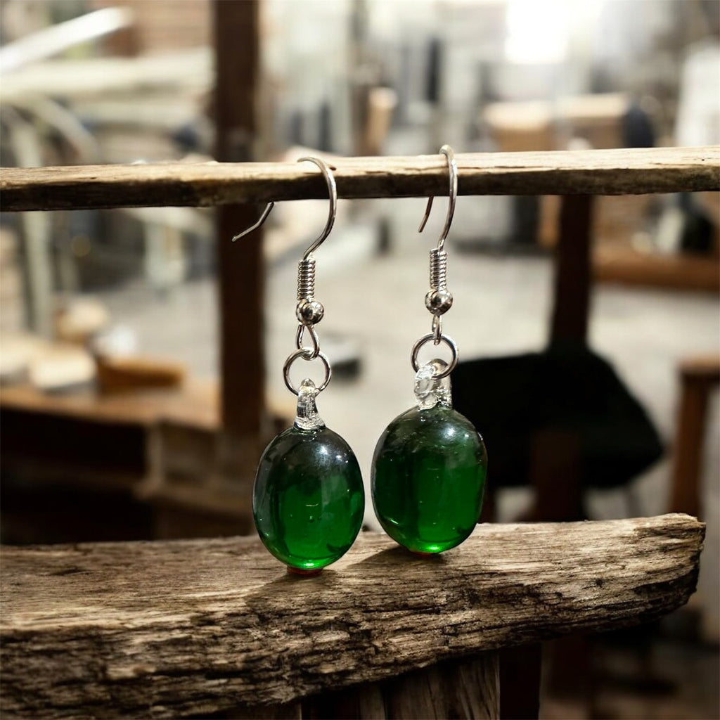 Green glass earrings on a wooden surface with a blurred background