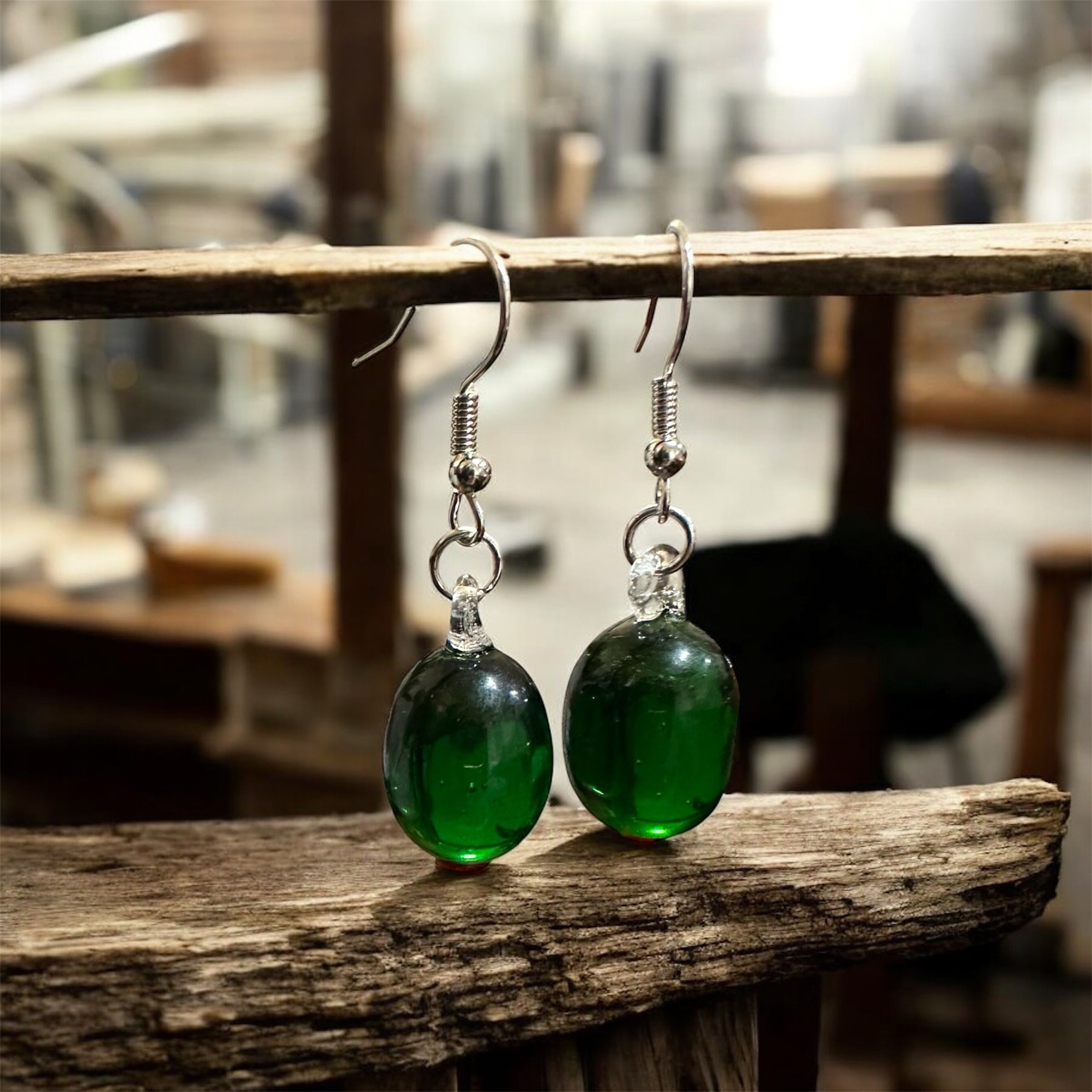 Green glass earrings on a wooden surface with a blurred background