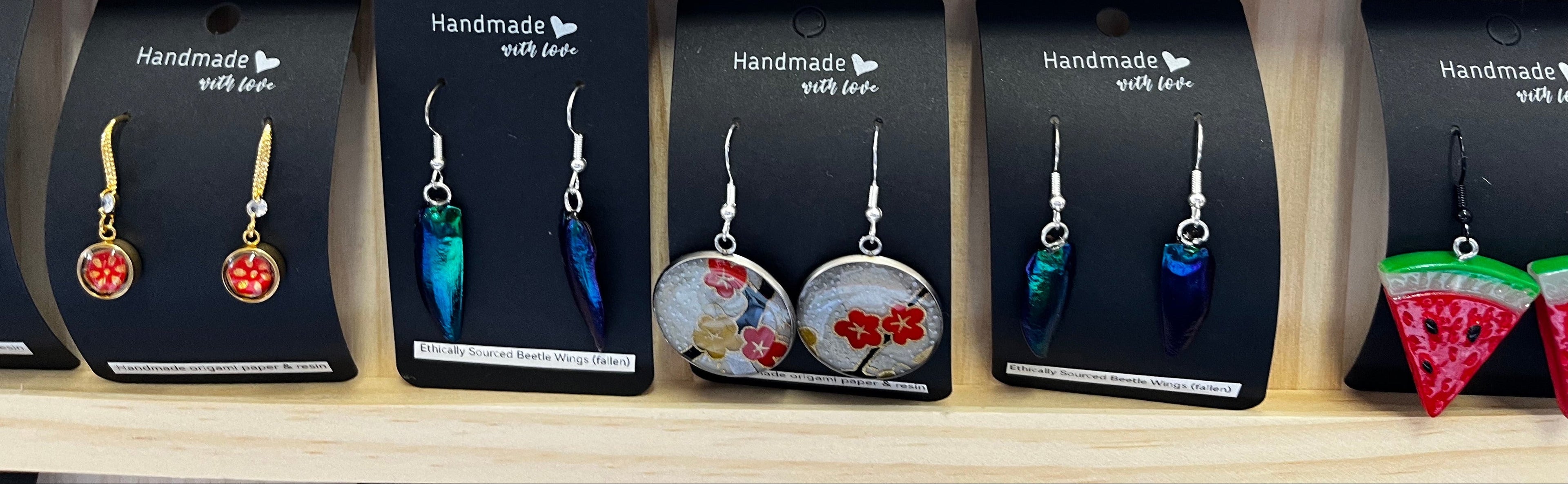 Display of handmade jewelry on black cards with 'Handmade with Love' text.